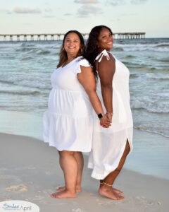 Sisters standing back to back holding hands on the beach.