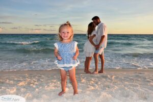 Little girl standing on the beach with her parents kissing behind her.
