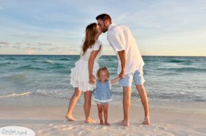 A couple kissing on the beach while holding their daughters hands