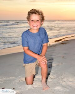 A little boy kneeling on the beach with the sunset behind him