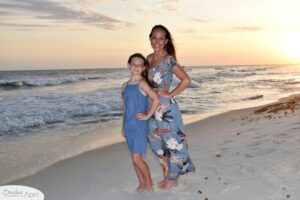 Mother and daughter standing on the beach with the sunset behind them