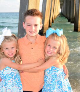 Boy with twin sisters smiling by the pier in Panama City Beach during a family photoshoot.