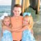 Boy with twin sisters smiling by the pier in Panama City Beach during a family photoshoot.