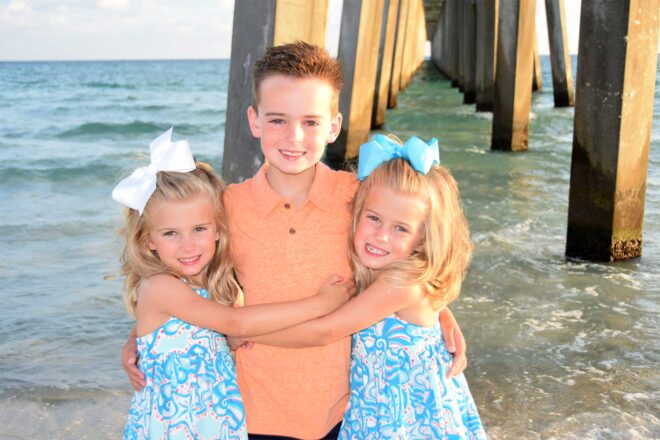 Boy with twin sisters smiling by the pier in Panama City Beach during a family photoshoot.