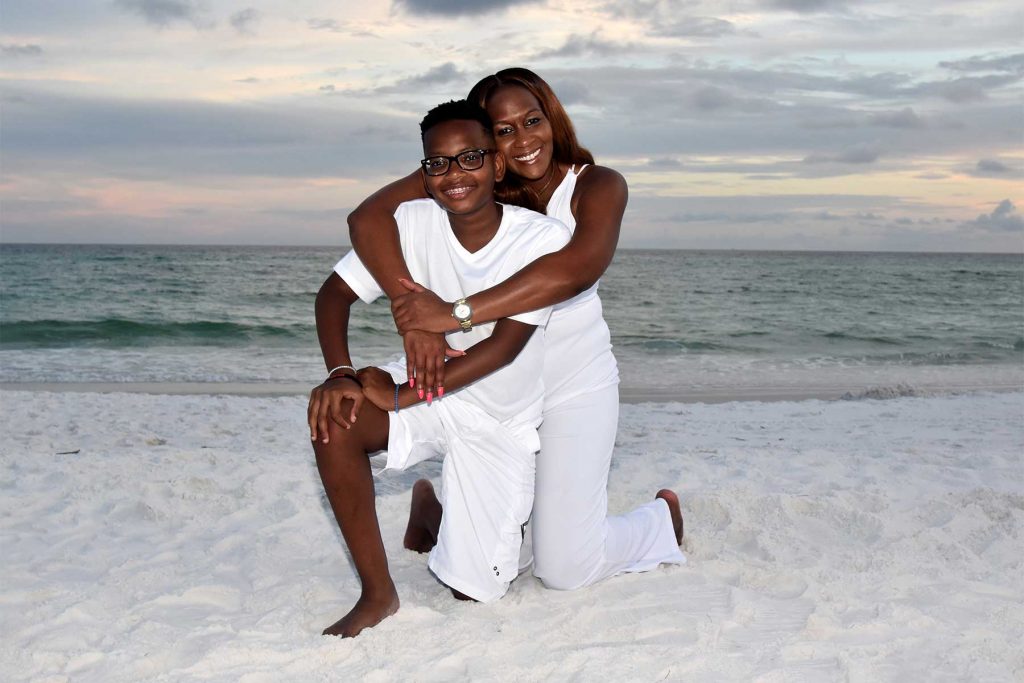A smiling couple with coordinated outfits with the water and sunset behind them on Panama City Beach.