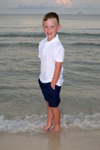 boy standing in waves at sunset