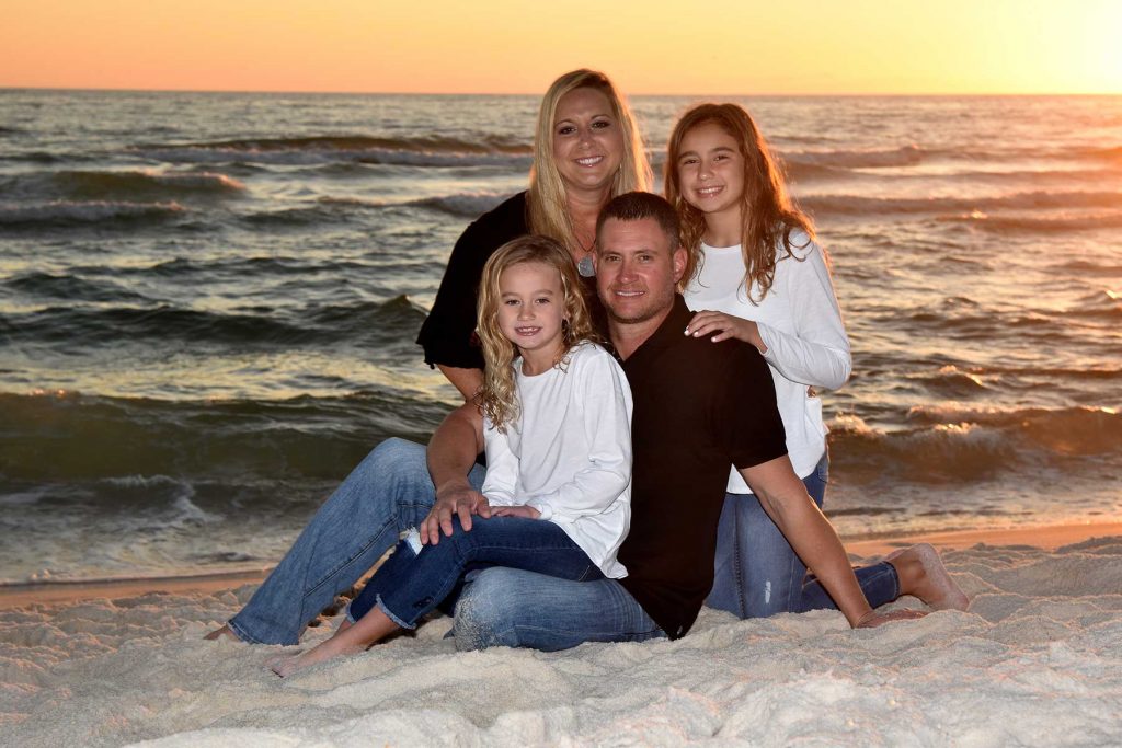 Family in blue and white outfits on the beach smiling for their Panama City Beach sunset photo