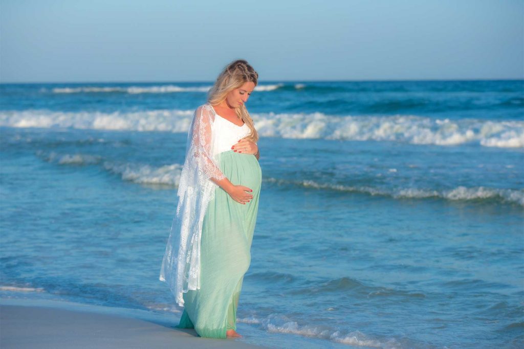 Woman walking through the water in Panama City Beach in her sunset maternity photo.