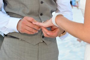 The groom putting the ring on the bride's finger during their beach wedding.