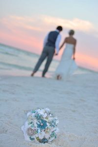 This photo shows the bride and groom walking down the beach towards the sunset. The bouquet is in the foreground.