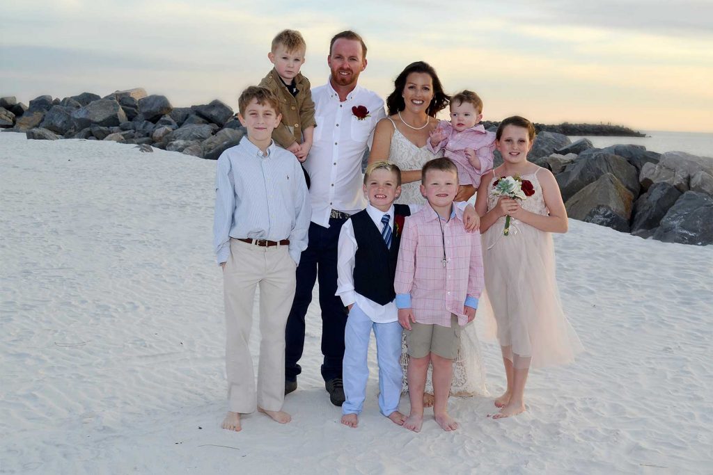 Family photos in St. Andrews State Park - on the sand with rocks, sea oats and the sunset behind them.
