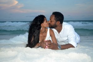 A newly married couple relaxes on the sand in front of a gorgeous sunset