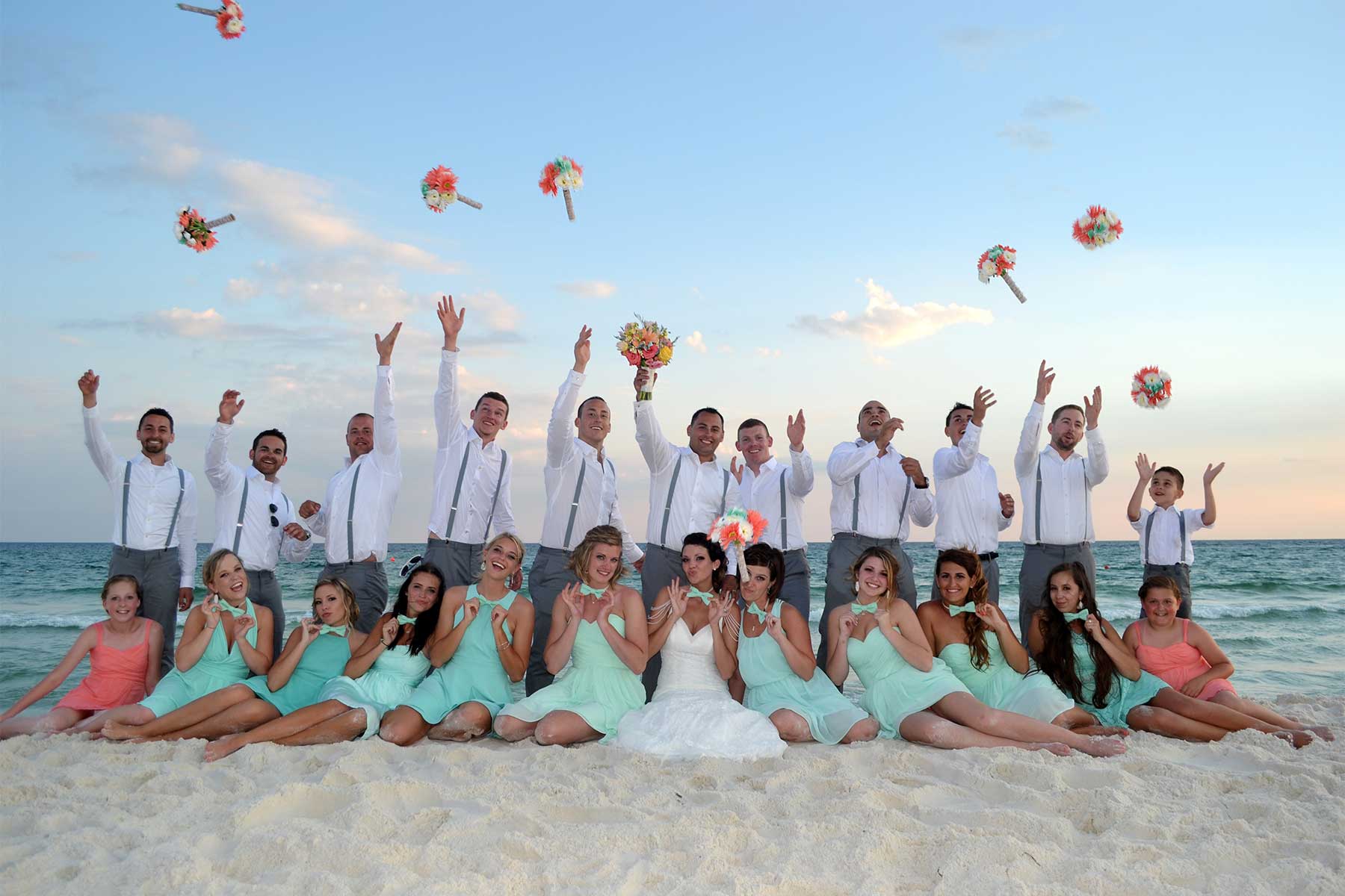 An action photo of the wedding party posed on the beach in front of a beautiful sunset.