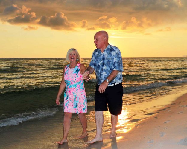 Older couple walking on the beach with a beautiful sunset behind them