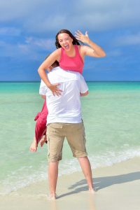 Photographer in PCB includes a fun pose for a young couple. She is showing the ring while he lifts her into the air.