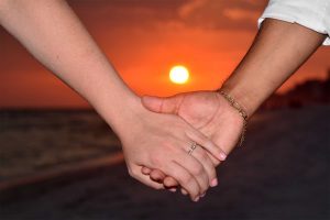 holding hands and ring in front of setting sun