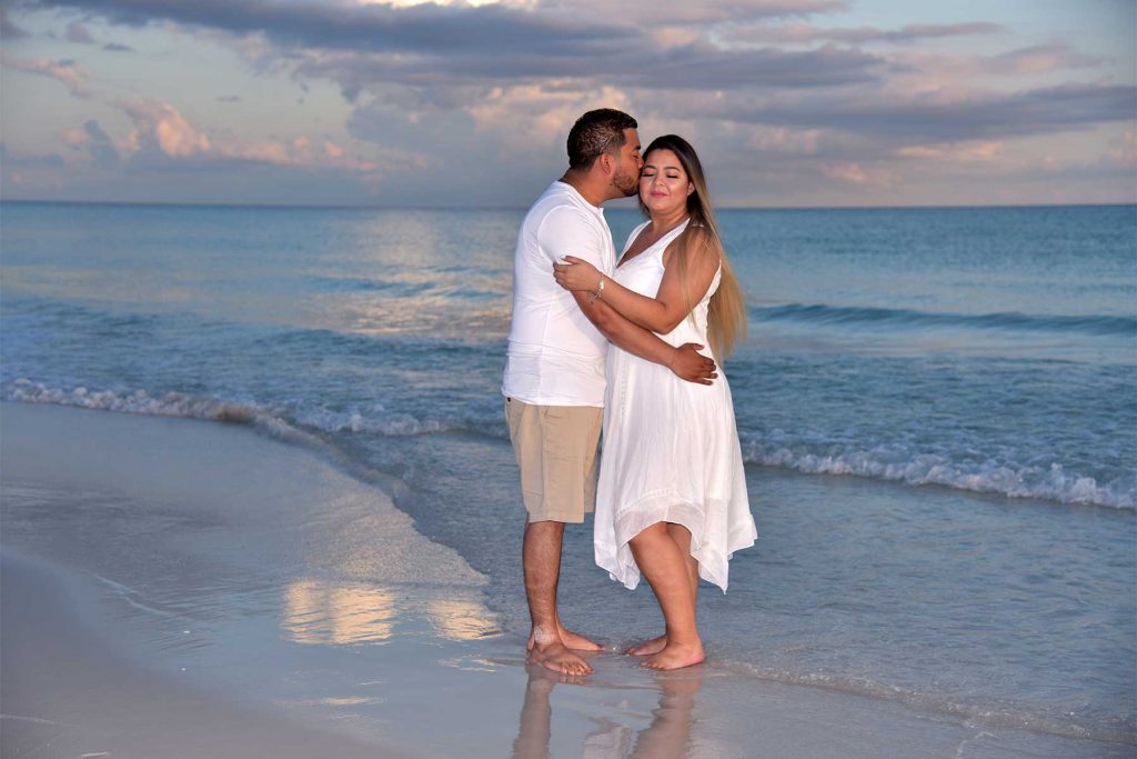 The couple kisses and poses in front of a beautiful beach sunset.