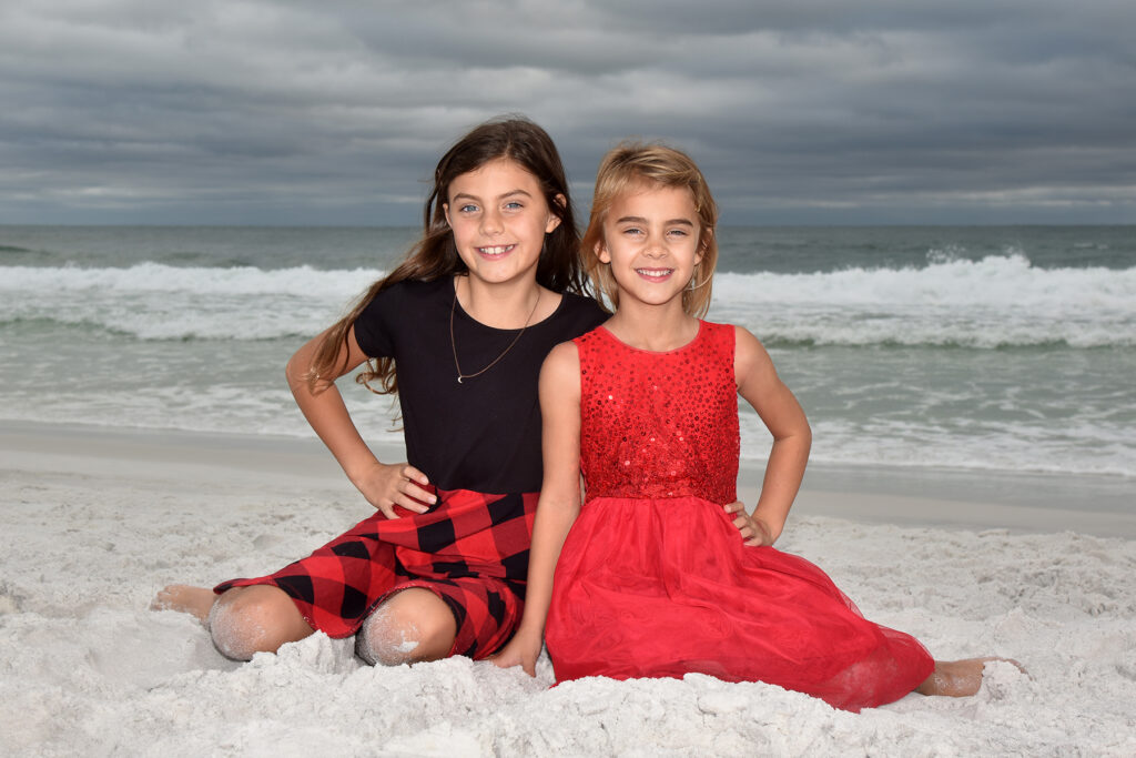 Two girls sitting on sand on Destin beach with waves behind them.